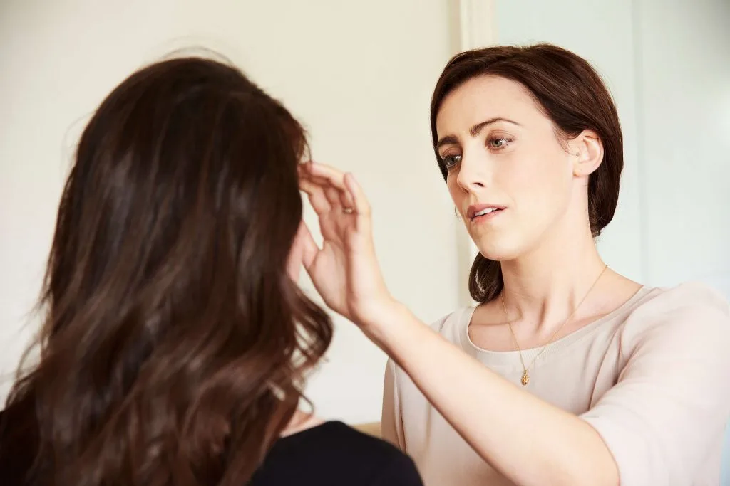 One woman gently tapping beside another woman’s eyebrow