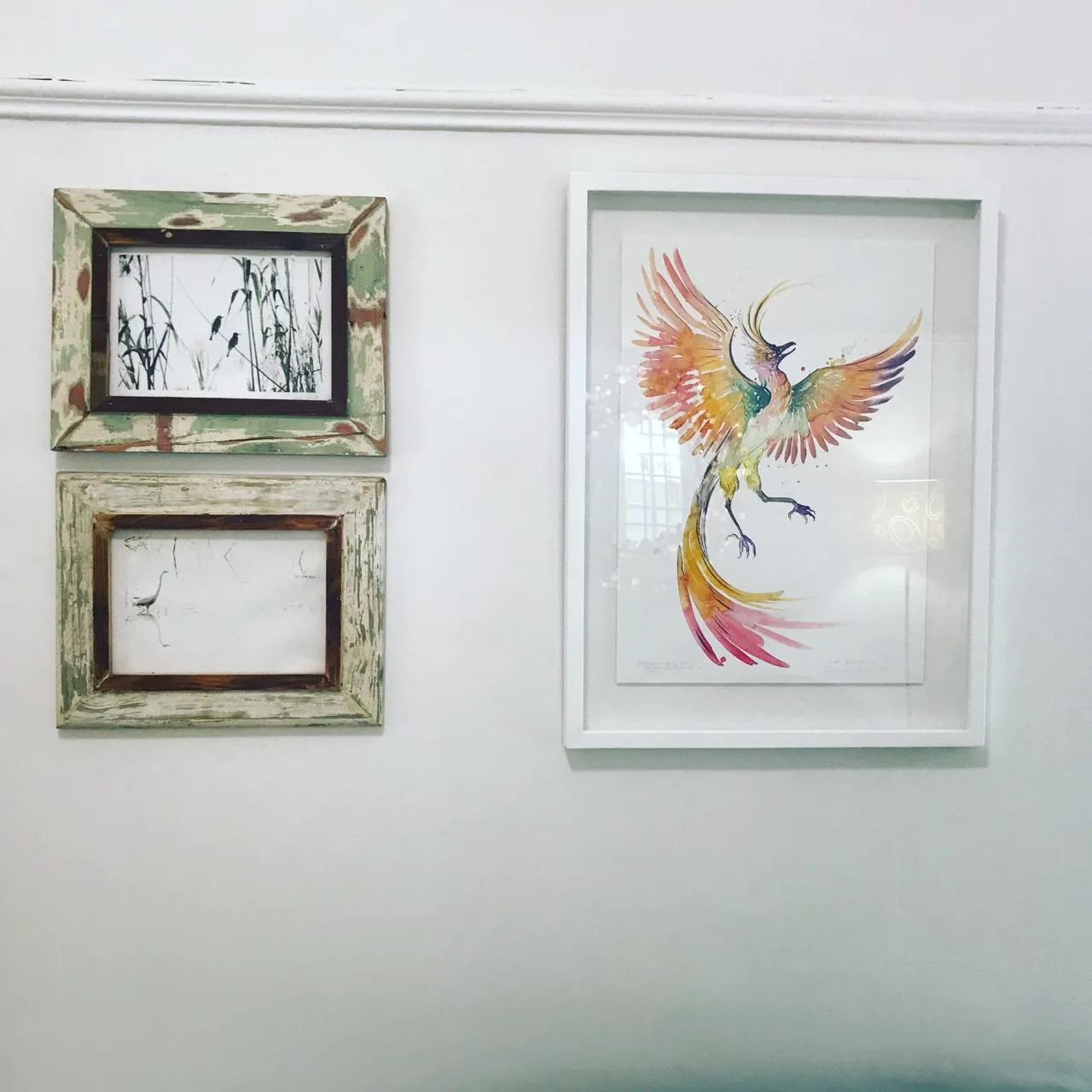 Renée’s phoenix painting in a white frame, beside two small framed pictures, on a wall of her consulting room