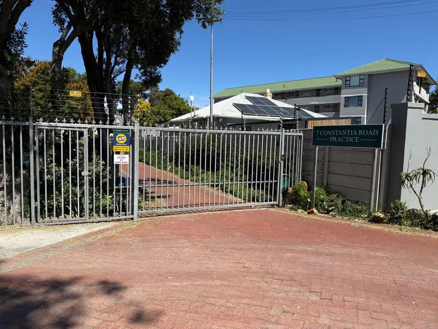 The grey street gate and red brick driveway of Renée’s practice, with the practice sign on the wall to the right